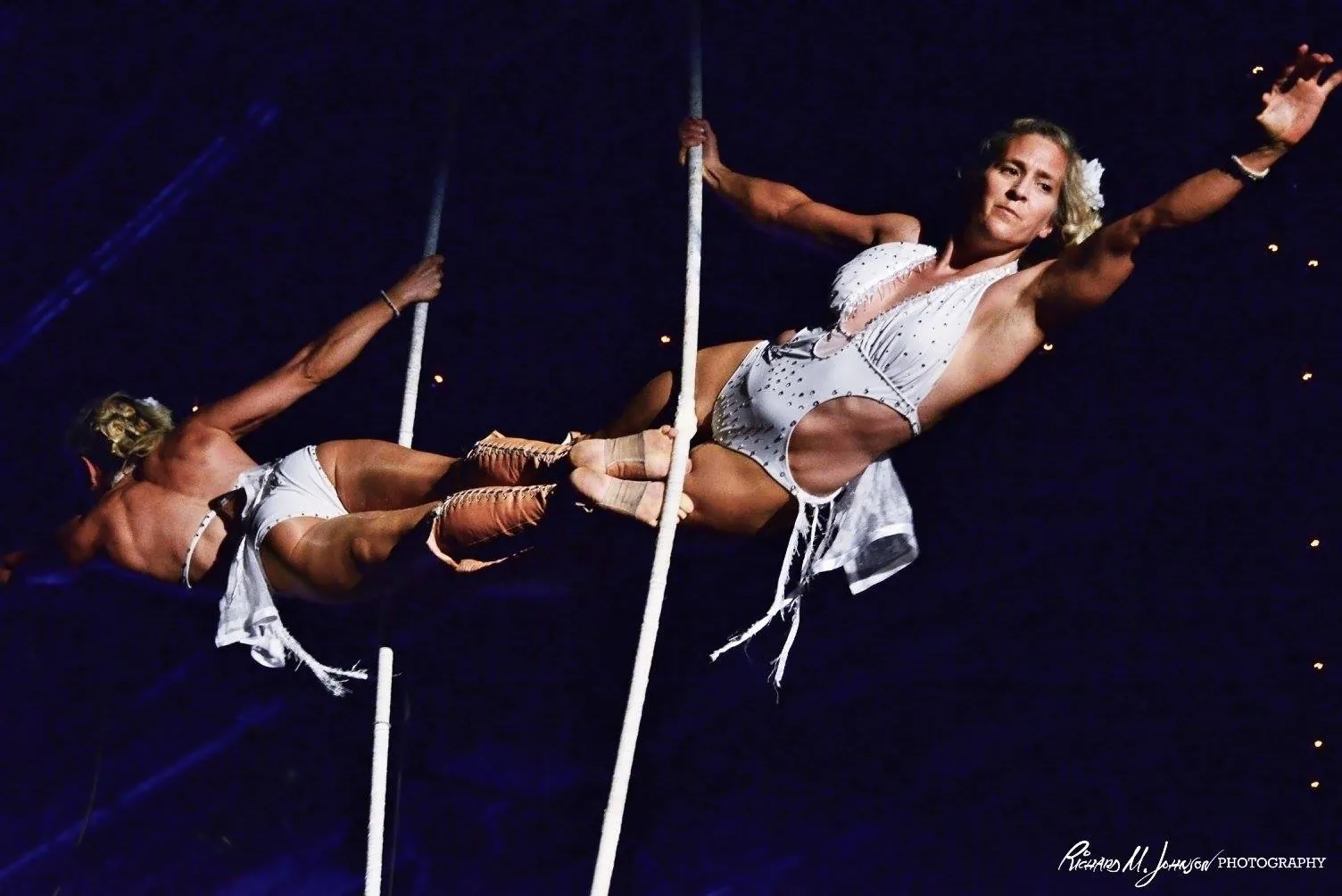 Two aerialists flying on a trapeze above the Fais Do-Do stage