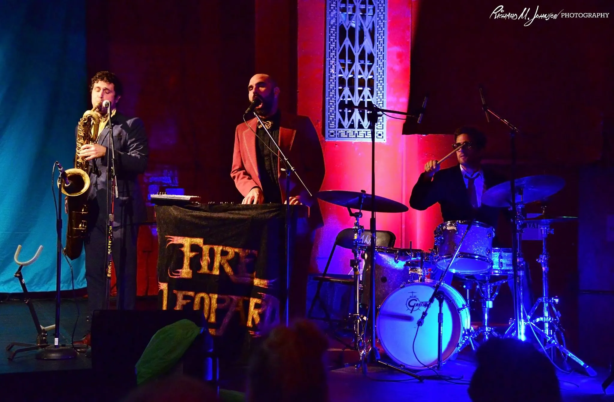 Live band with saxophone, keys and drums under the red stage curtains