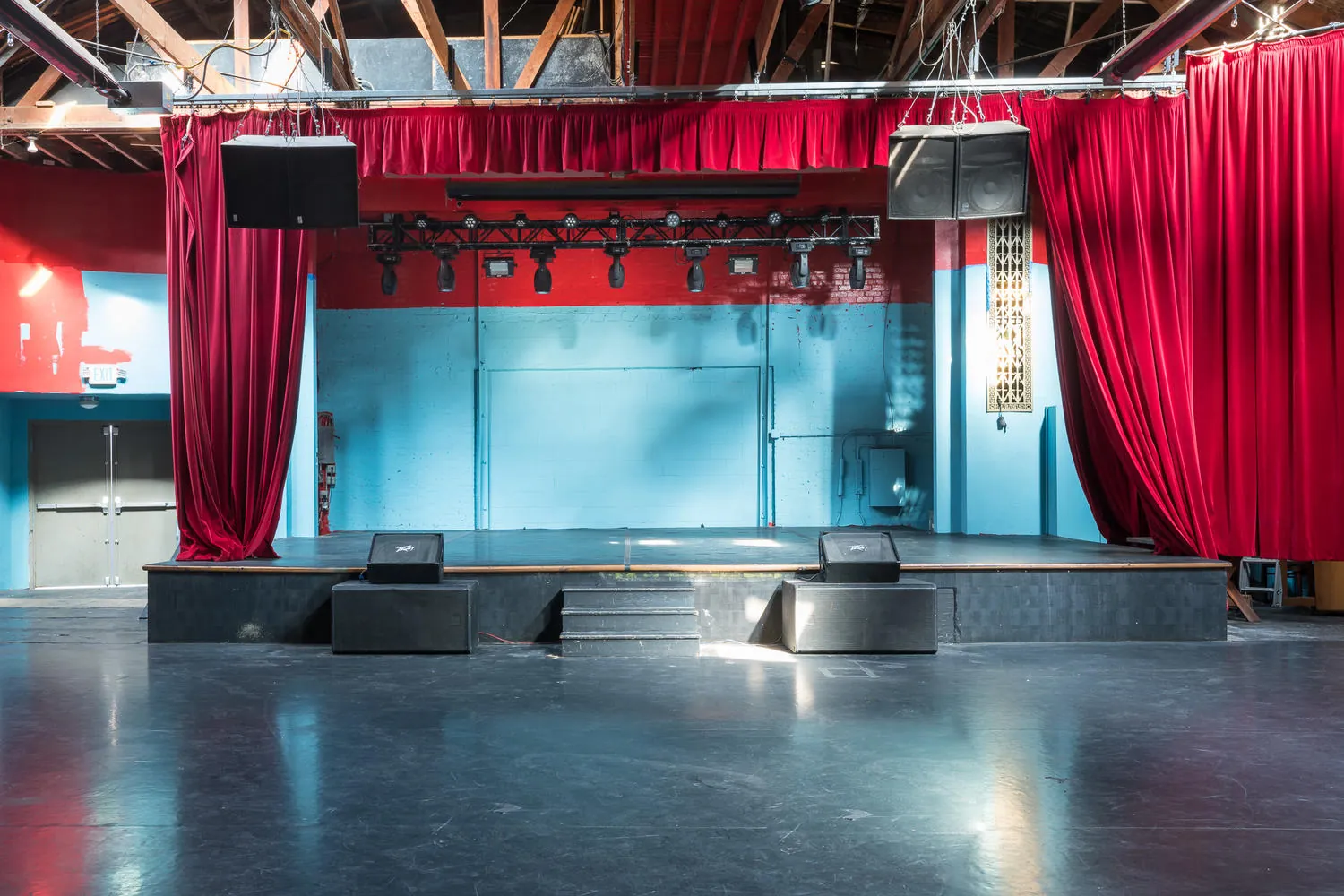 Empty platform stage framed by red curtains and a lighting truss